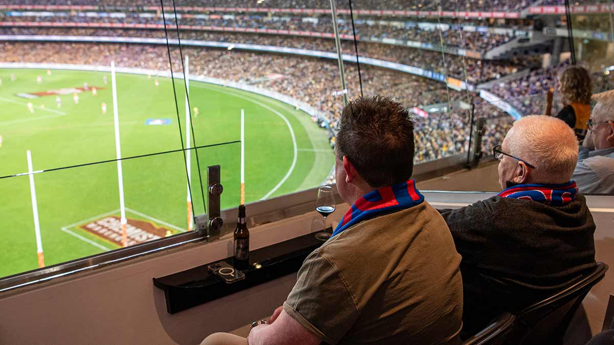 Two men watching footy in corporate suite at MCG