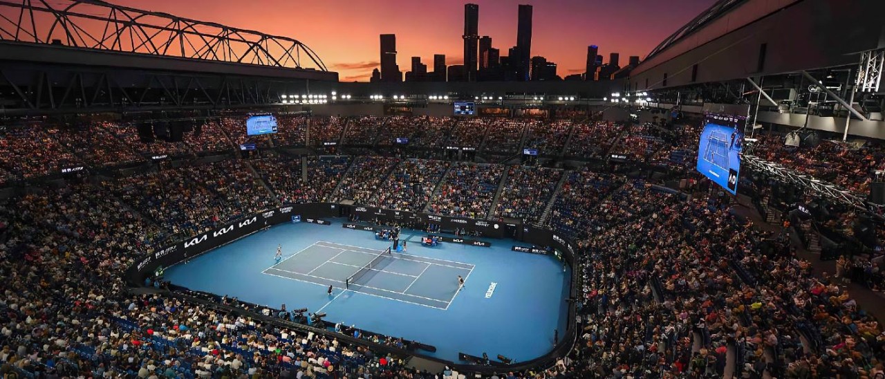 large crowd watching tennis at sunset with city skyline in background