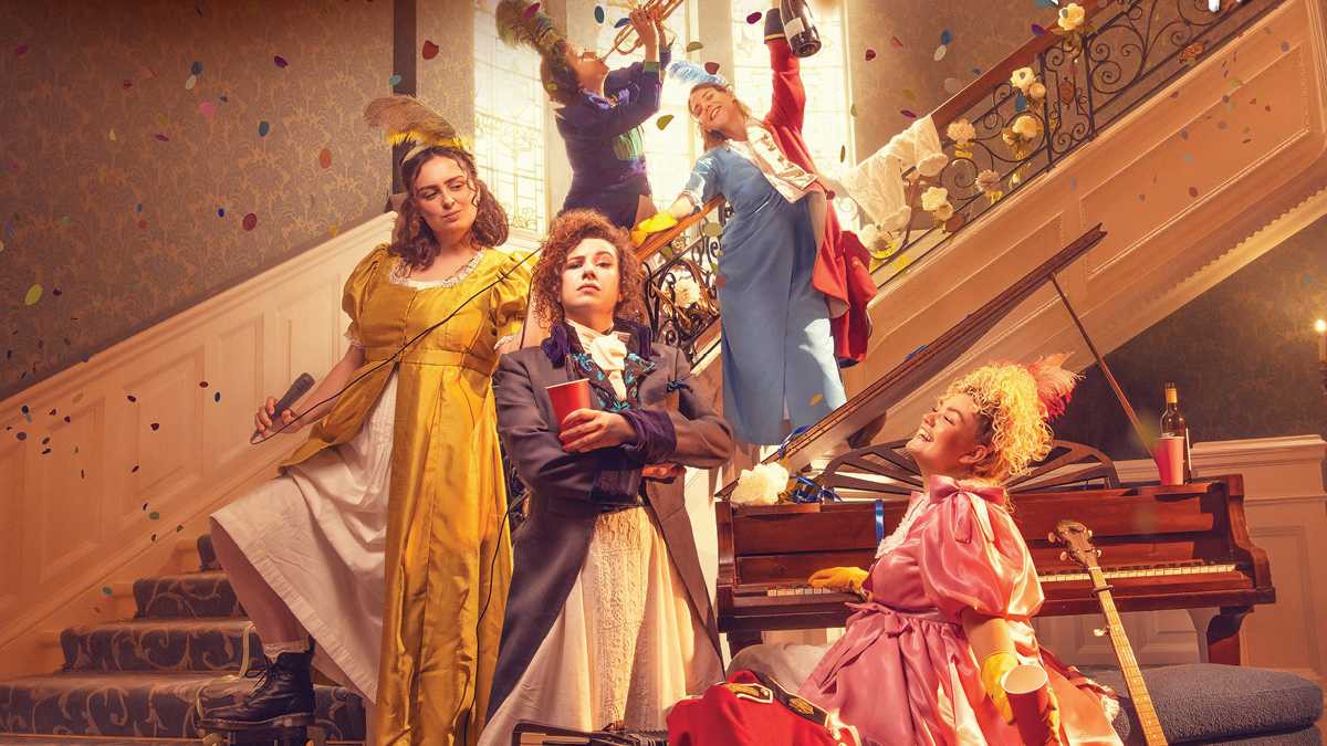five women dressed in wigs playing instruments and holding drinks in an opulent home