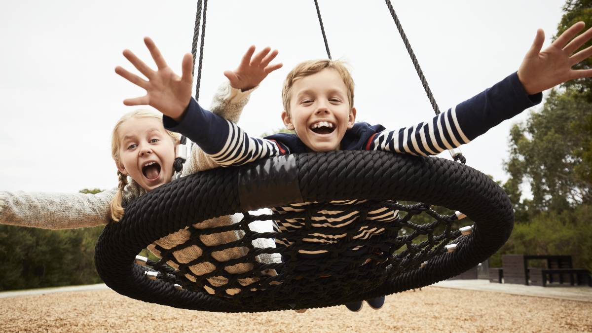two kids riding on swing in playground
