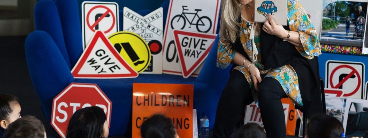 woman teaching seated children about safety with various road signs