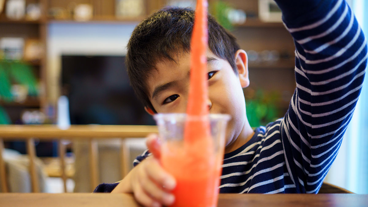 child playing with orange slime science experiment in cup on wooden table