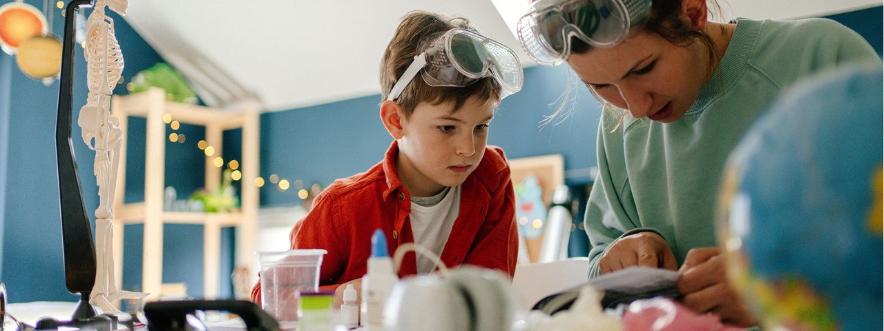 1214330735 child and adult with safety googles in classroom doing science experiement