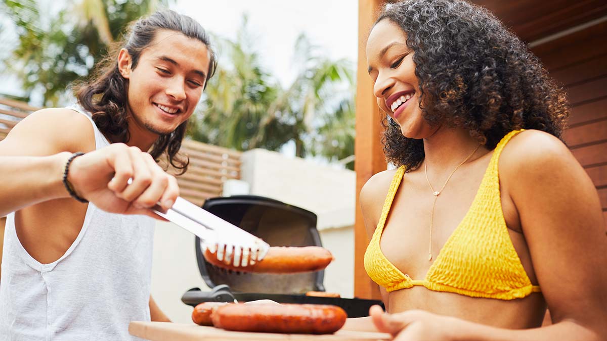 Young man serving up sausages at BBQ with female companion