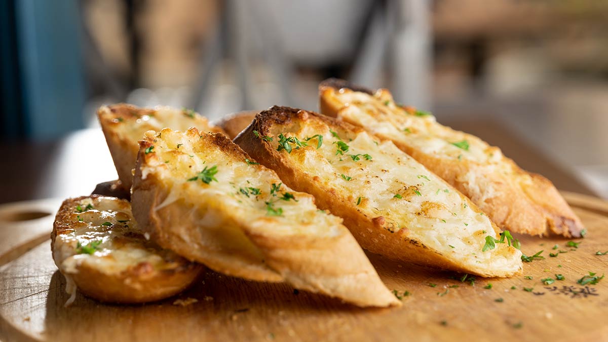Four slices of garlic bread artfully arranged on a wooden board