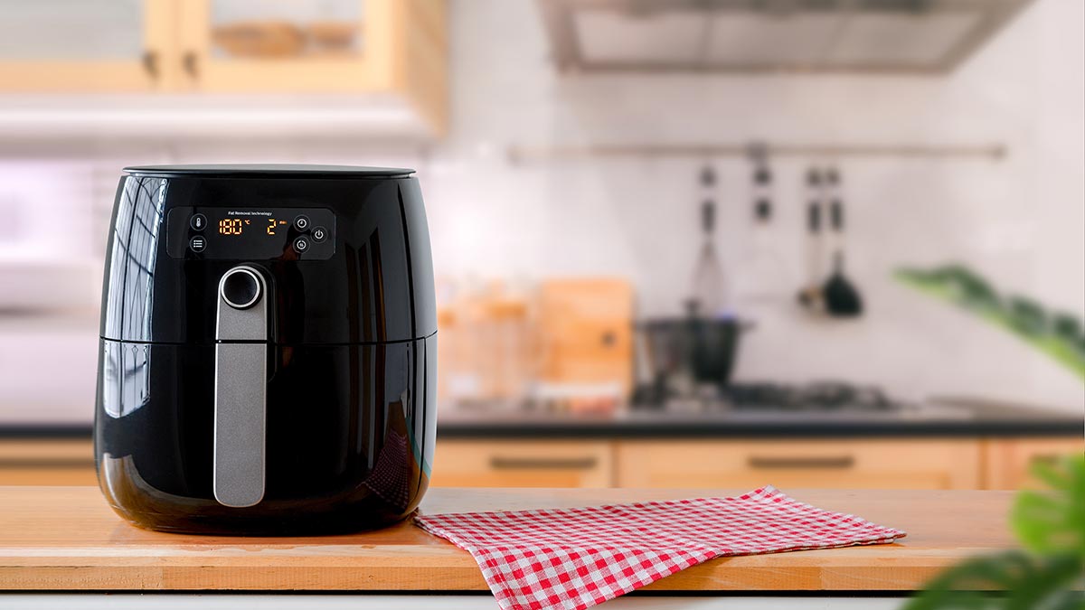 Air fryer on kitchen bench next to red-and-white checkered napkin.