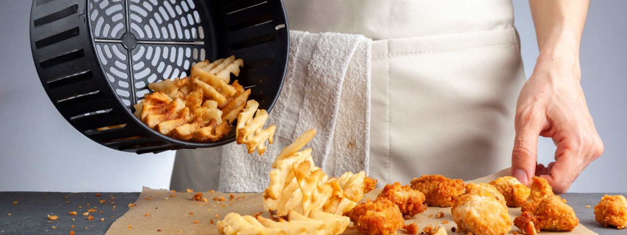 1305594718 air fryer basket full of potato chips poured onto tray