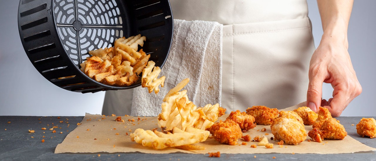 Chips and chicken nuggets being tipped out of air fryer basket onto baking paper.