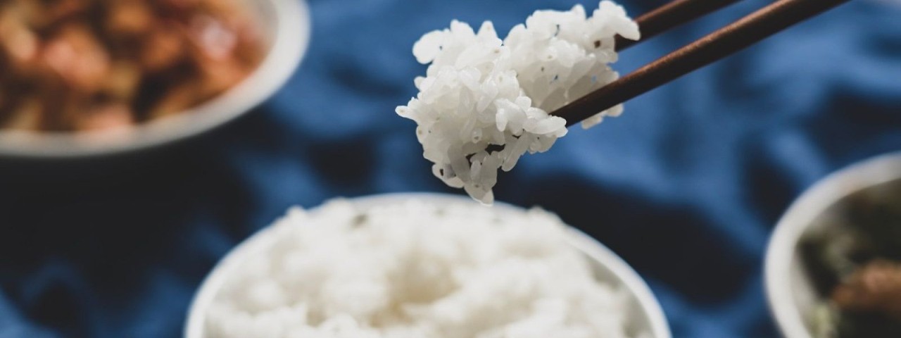 chopsticks holding a portion of cooked white rice against a blue tablecloth