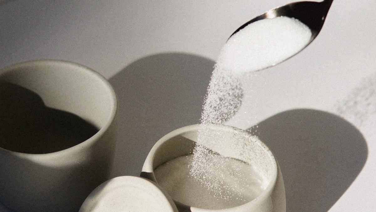 spoonful of white sugar being poured into a small ceramic jar