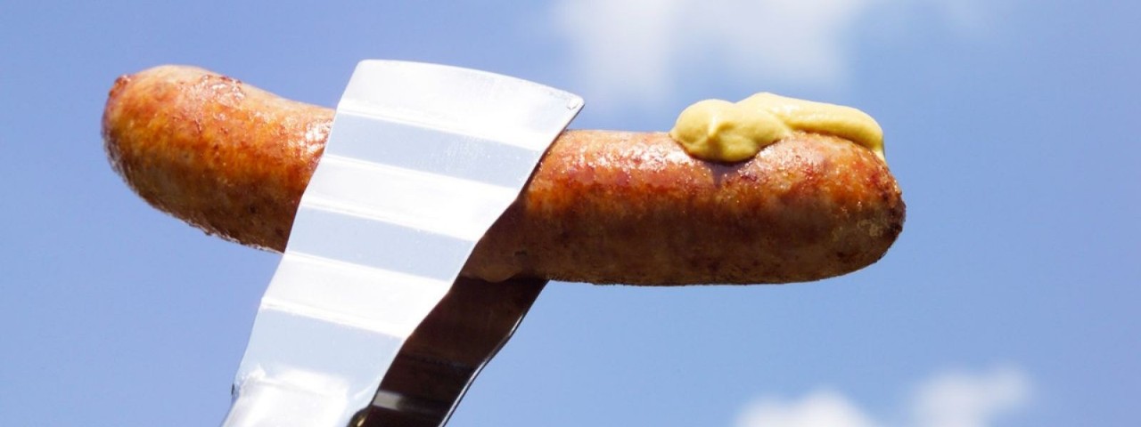 silver tongs holding a sausage and mustard