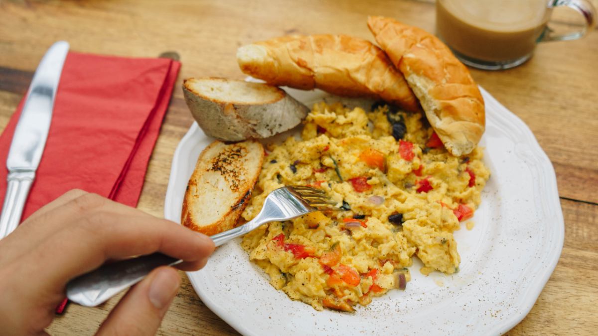 Scrambled eggs with vegetables and toast and hand with fork on left hand side.