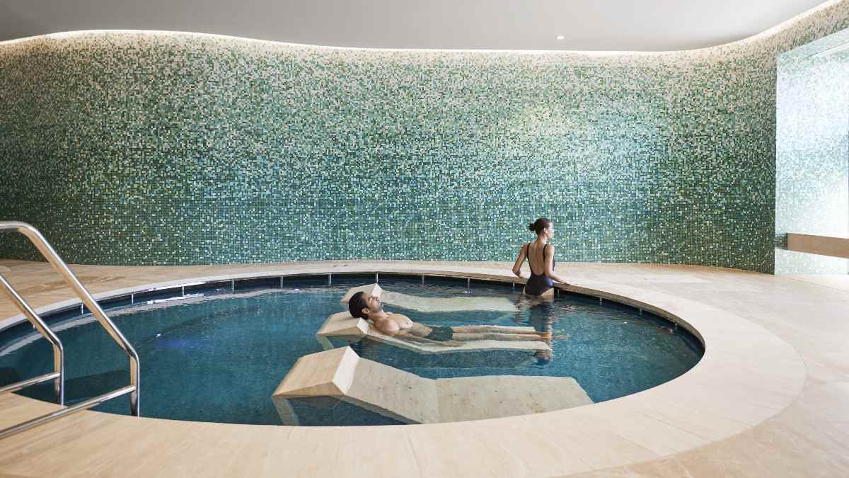 man lying on hammam recliner while woman stands in pool