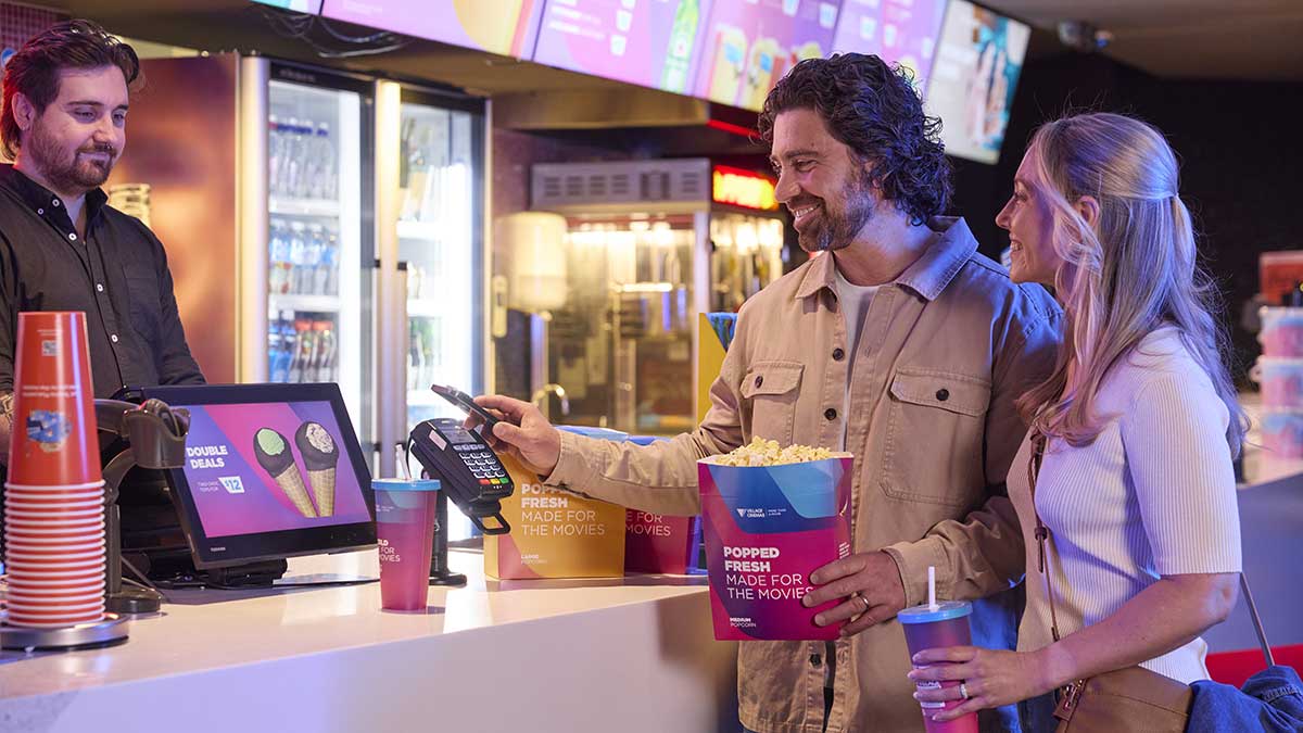 Couple purchasing snacks and movie tickets in cinema.