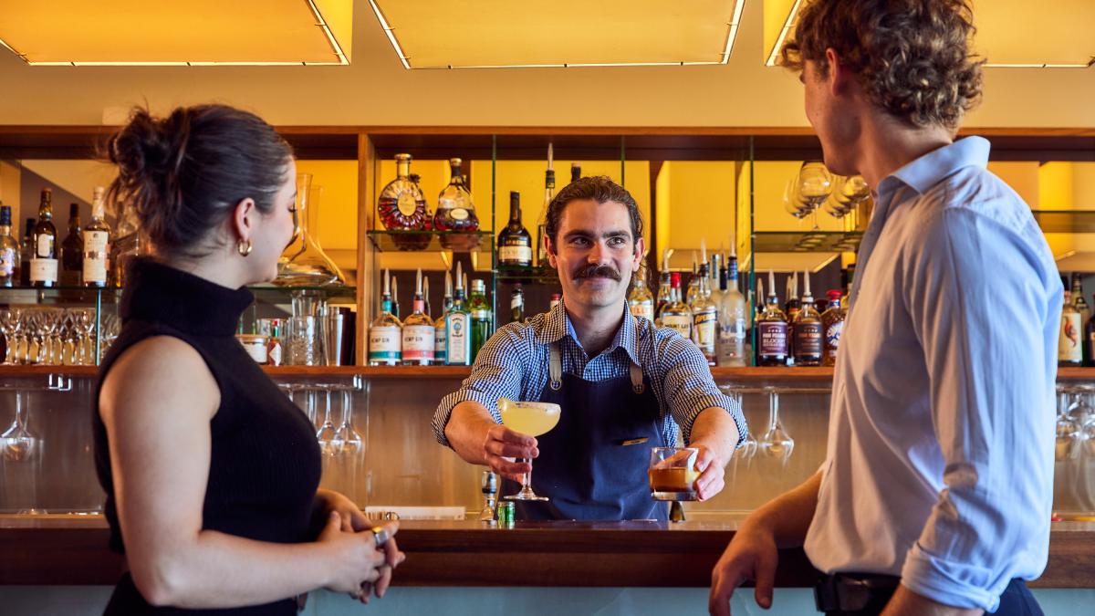 A man and a woman being handed two drinks by the bartender at Zenith Lounge and Bar at RACV Inverloch