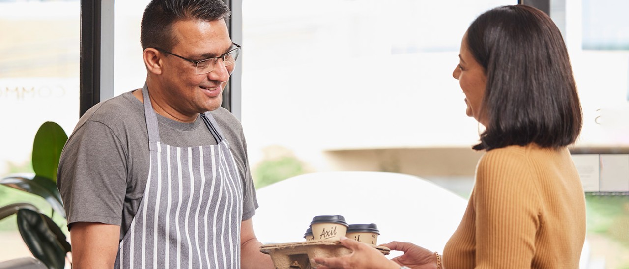Store owner handing tray of coffees to customer