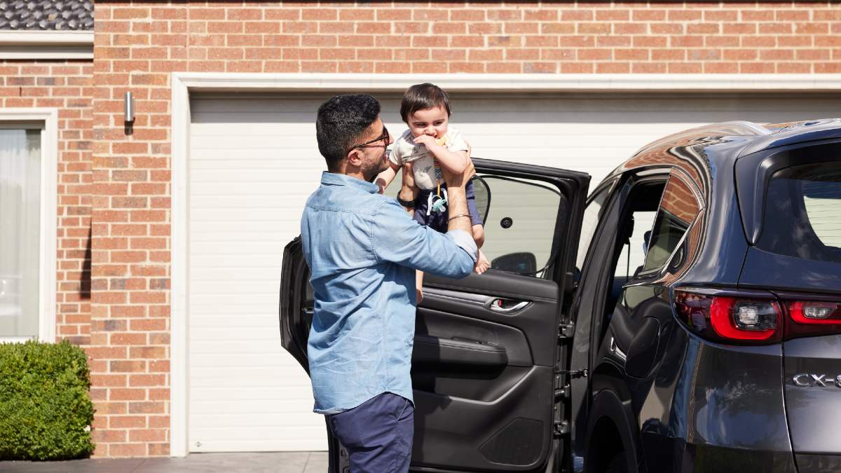 father putting son in backseat of car in front of garage door