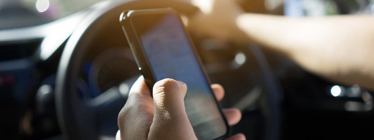 Person holding mobile phone in car while driving