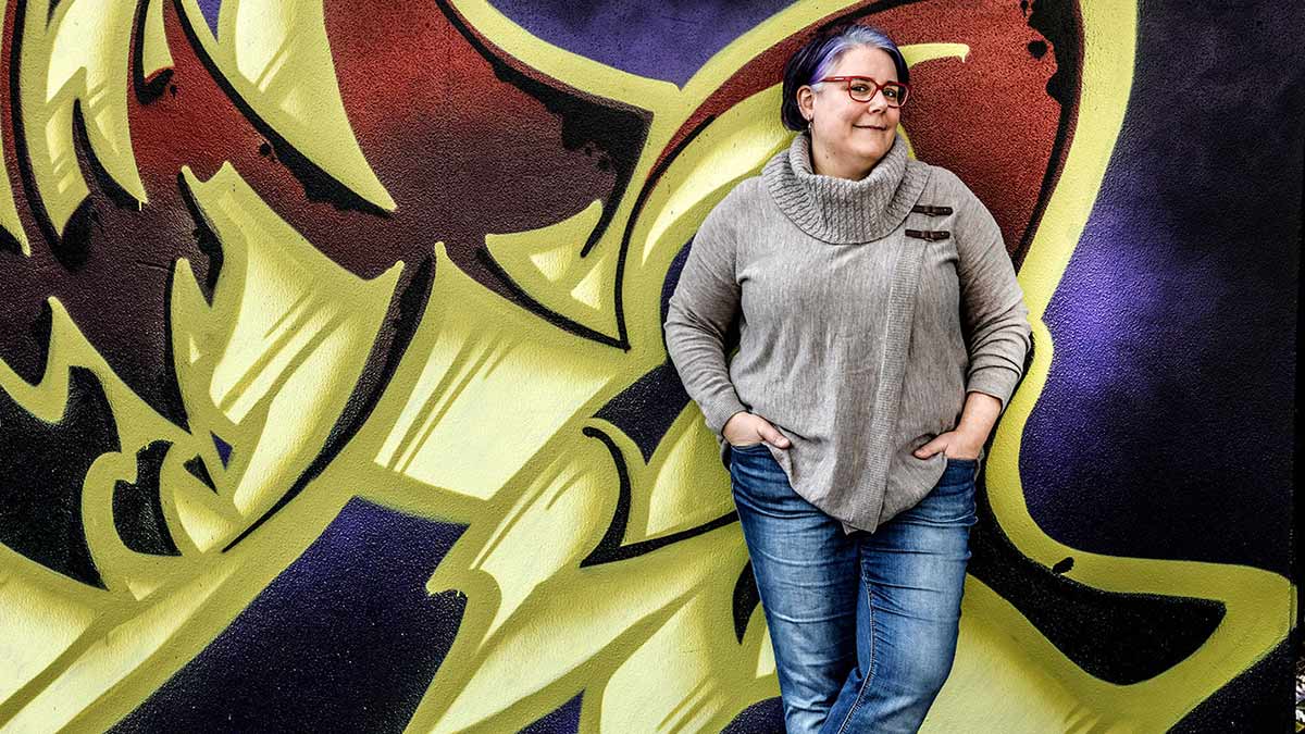 Woman standing up leaning against graffiti covered wall.