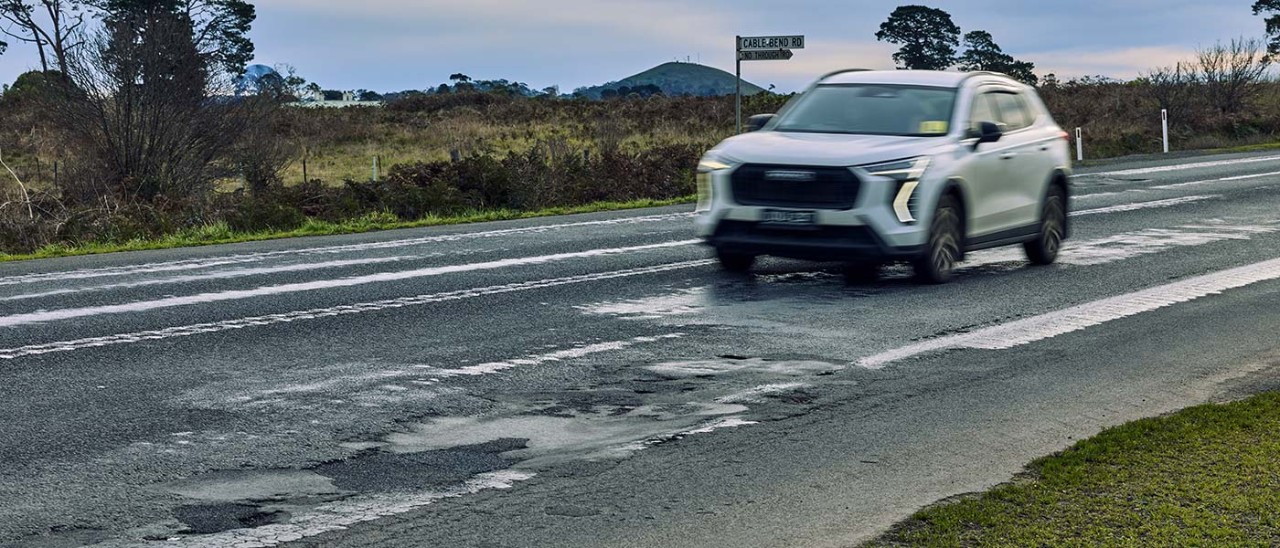 A white SUV driving along a rough section of road between Colac and Camperdown on the Princes Highway
