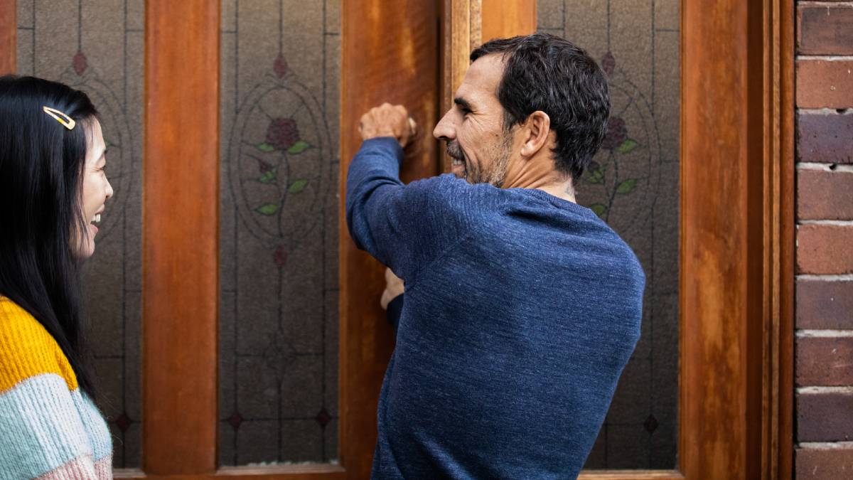 A man locking a front door while a woman watches on smiling