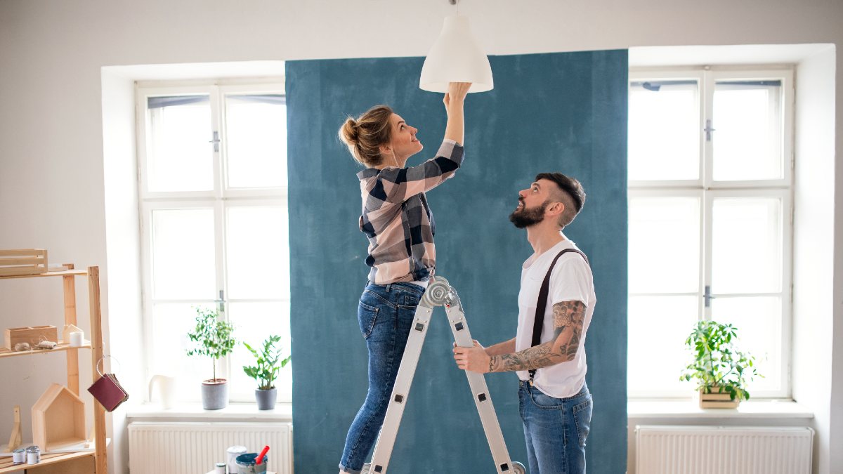young couple changing a lightbulb on a ladder