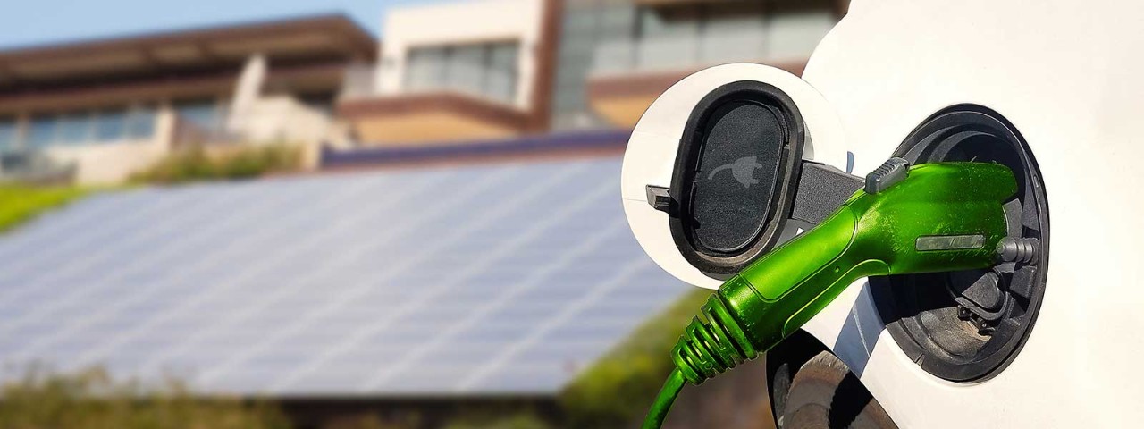 Electric vehicle charging pump with solar panels in background.