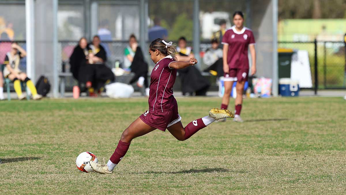 Female football player about to kick round ball.