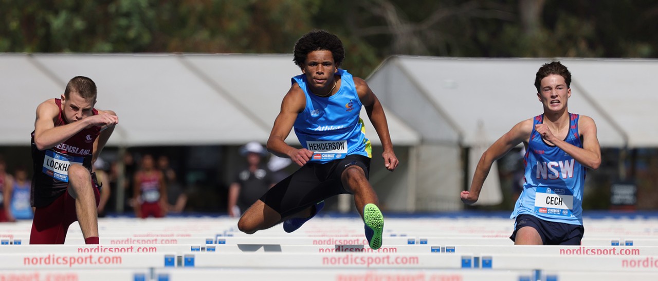 Three young men competing in hurdles race.