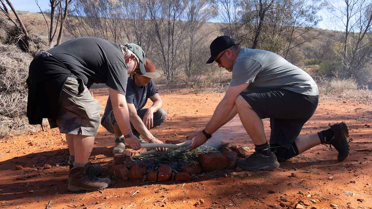 Three people build a campfire at a Yalari Outback Camp experience in Australia.