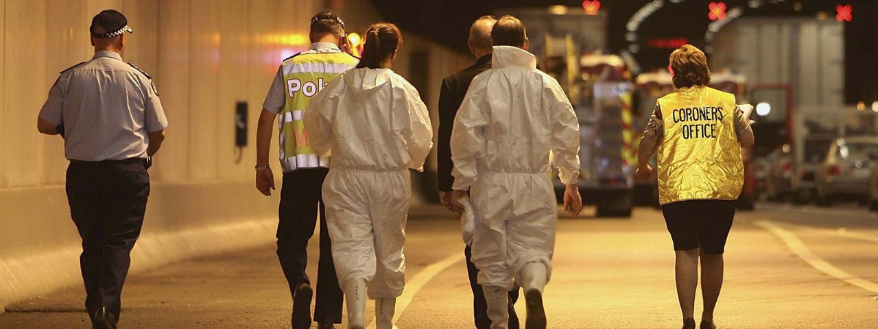 Police offers and coroner walking towards a firetruck in a tunnel