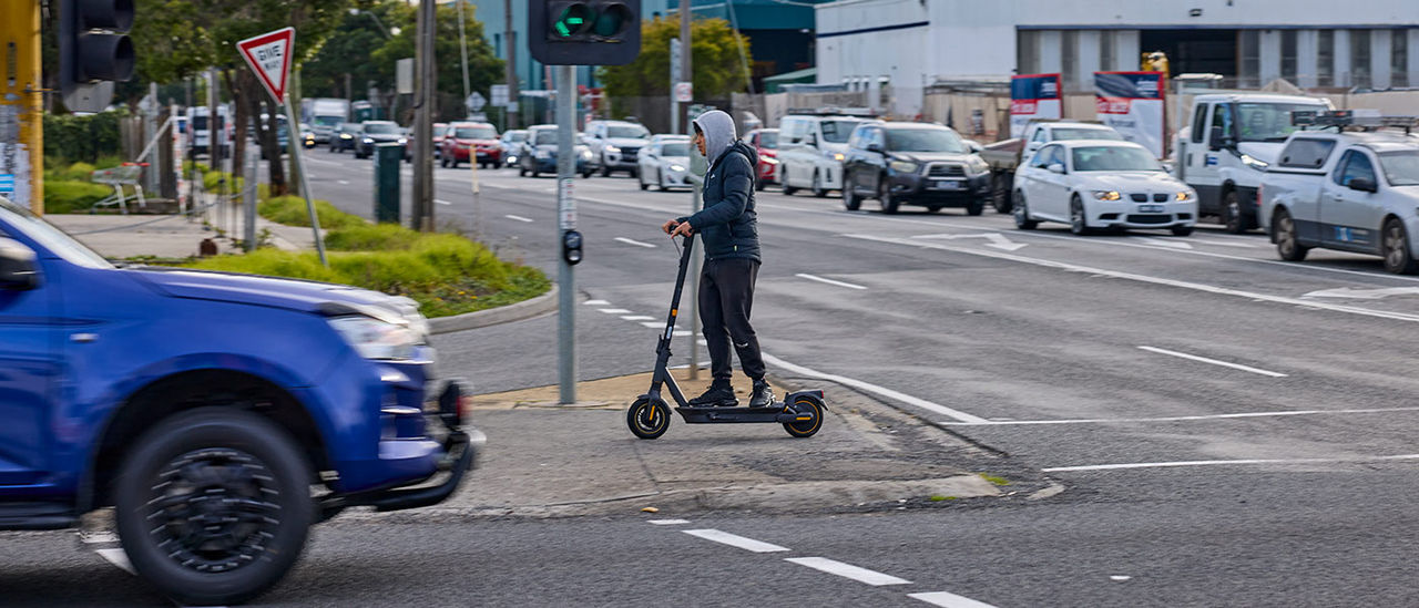 A young person riding an escooter across the intersection of Springvale Rd and Princes Highway in Mulgrave