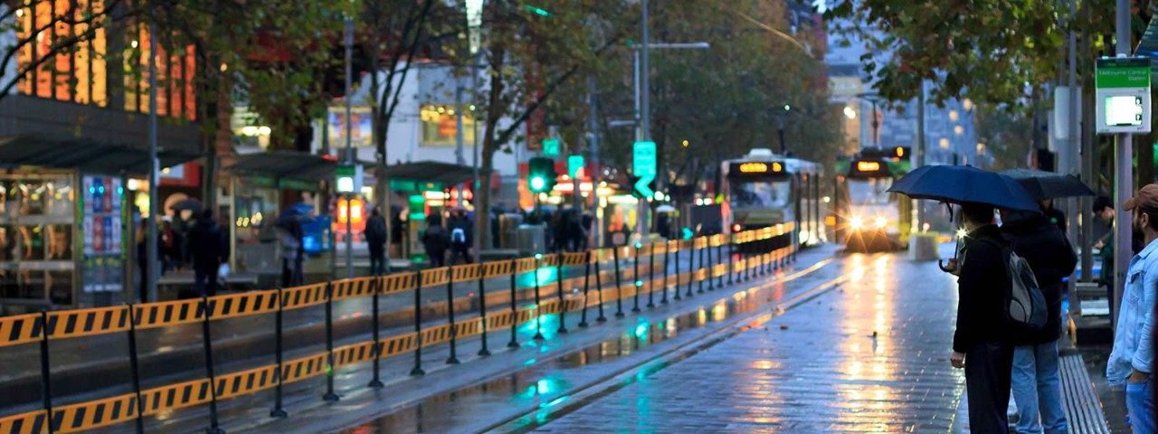 People wearing suits waiting for tram in Melbourne while holding umbrellas