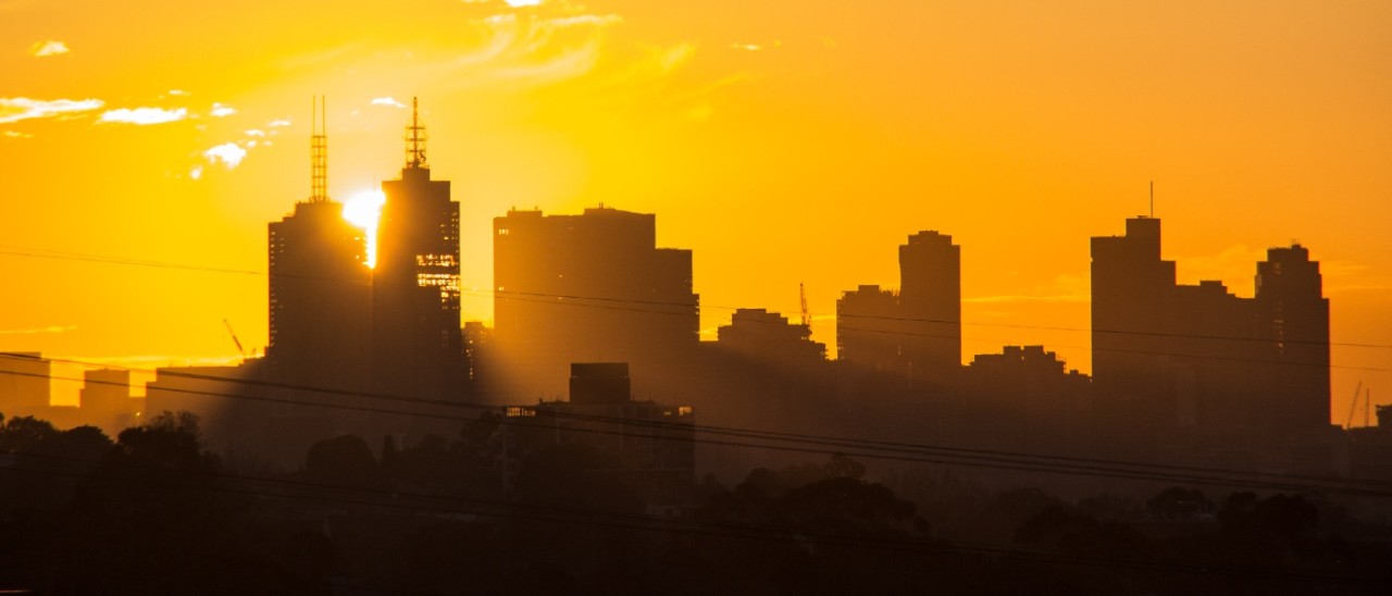A large yellow sun setting behind the Melbourne city skyline, lighting up the sky in bright orange after a hot day