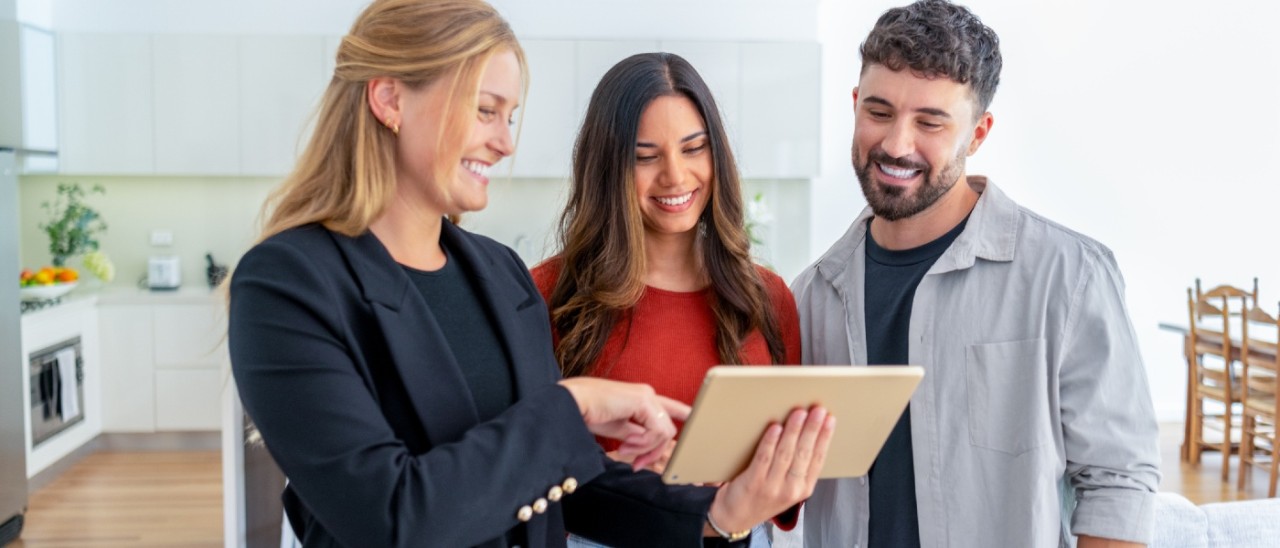 A couple looking happily at a digital tablet held by a sales person in a display home for off-the-plan homes