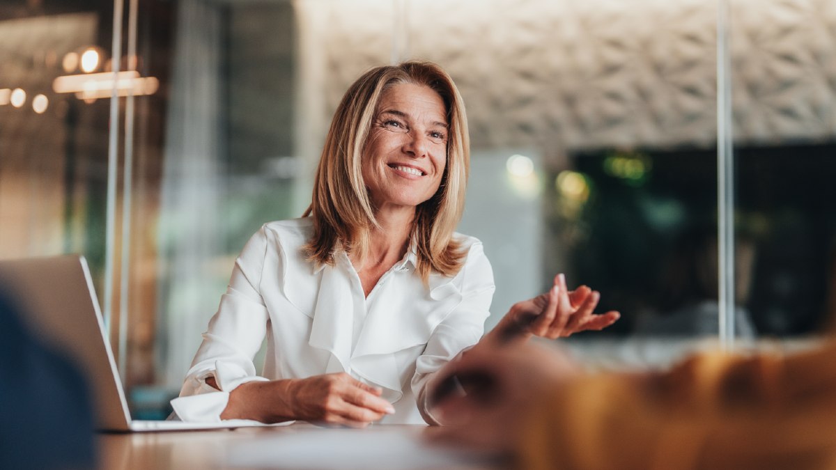 real estate agent smiling and gesturing as she talks to someone while sat at a table