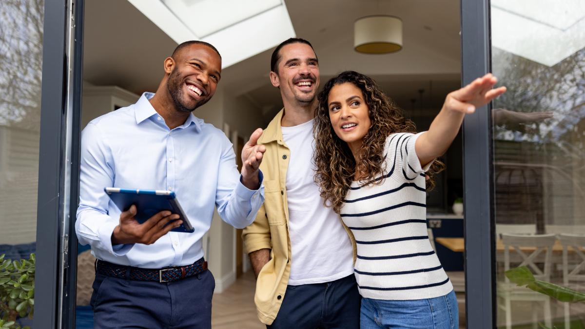 real estate agent holding tablet and smiling as two homeowners show him something in the backyard