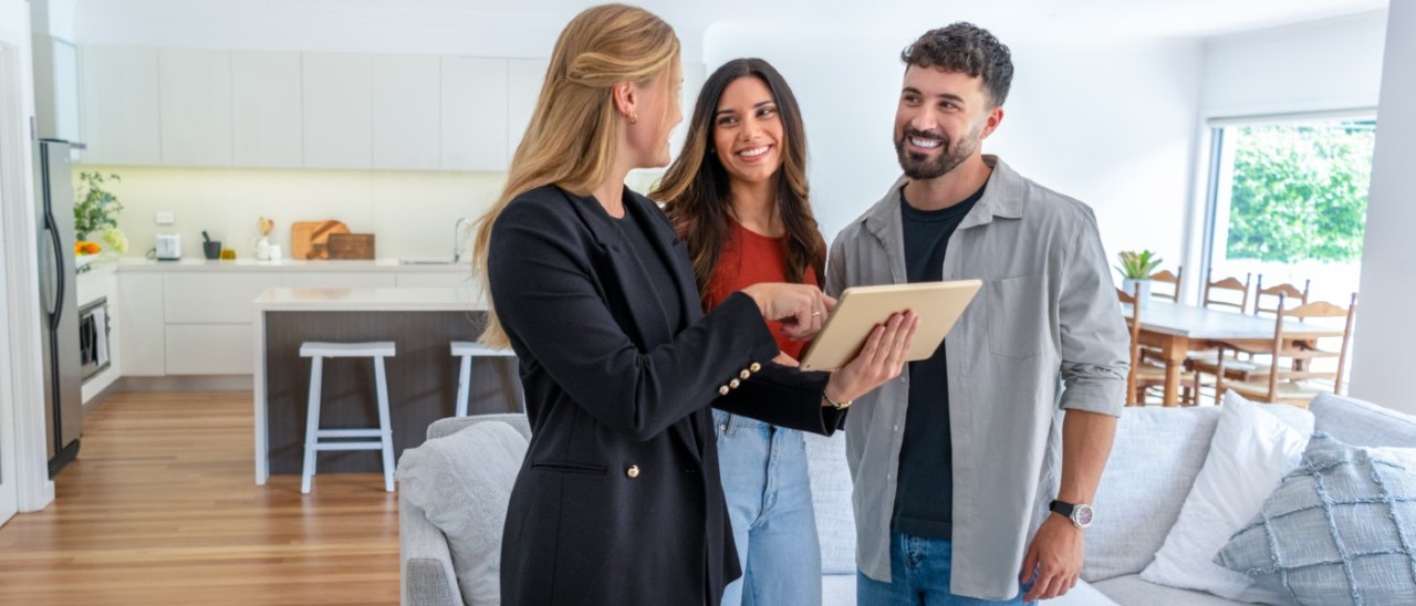 real estate agent showing two homeowners something on a tablet in their home