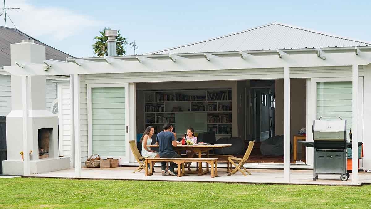 family sitting in outdoor undercover home area with open doors next to lawn