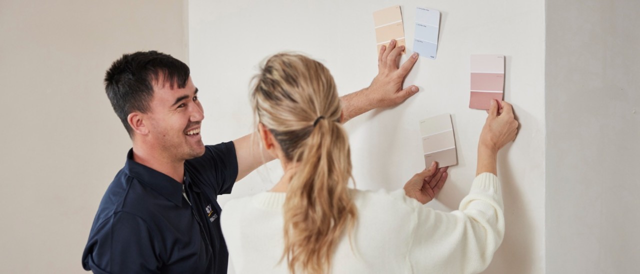 RACV tradie comparing paint samples on a wall with homeowner