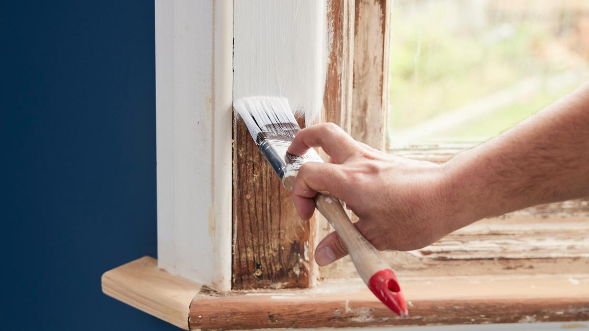 A person painting a wooden window sill white