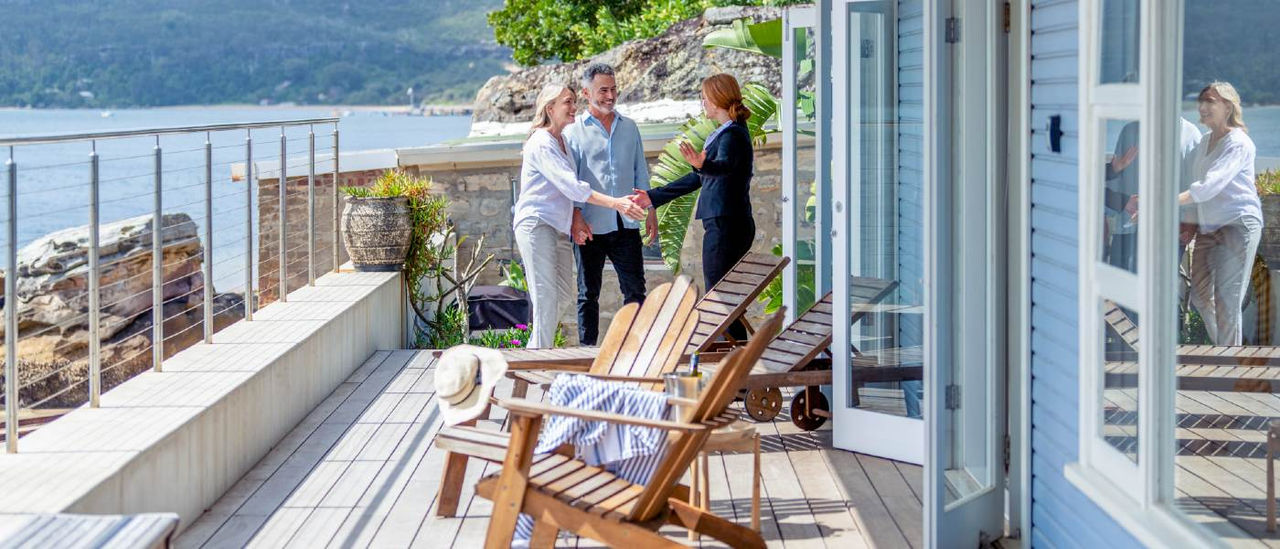 real estate agent shaking hands with older couple in porch of home fronting water