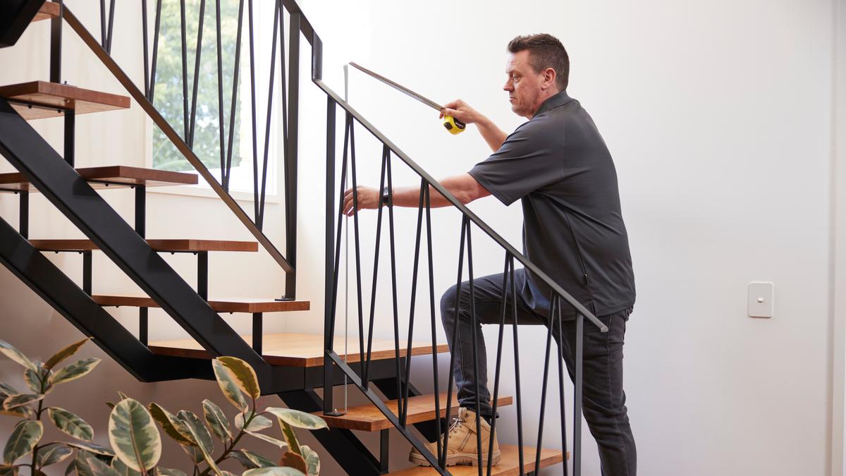 A property inspector measuring the handrail on an internal staircase