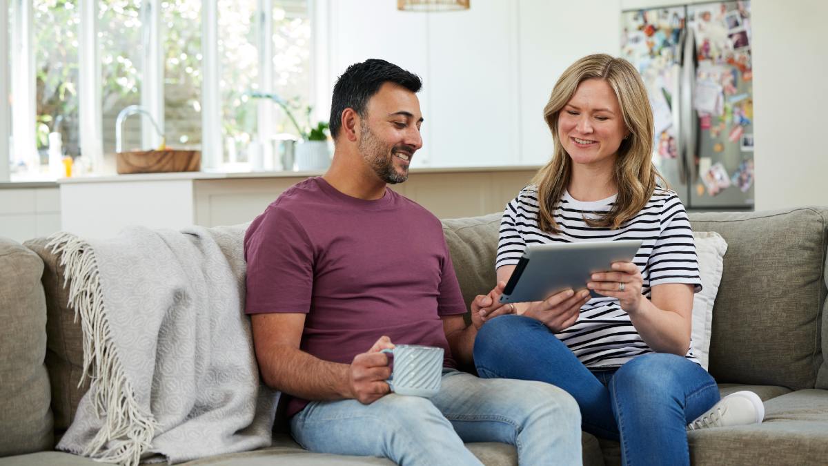 young couple on couch looking at a tablet and smiling