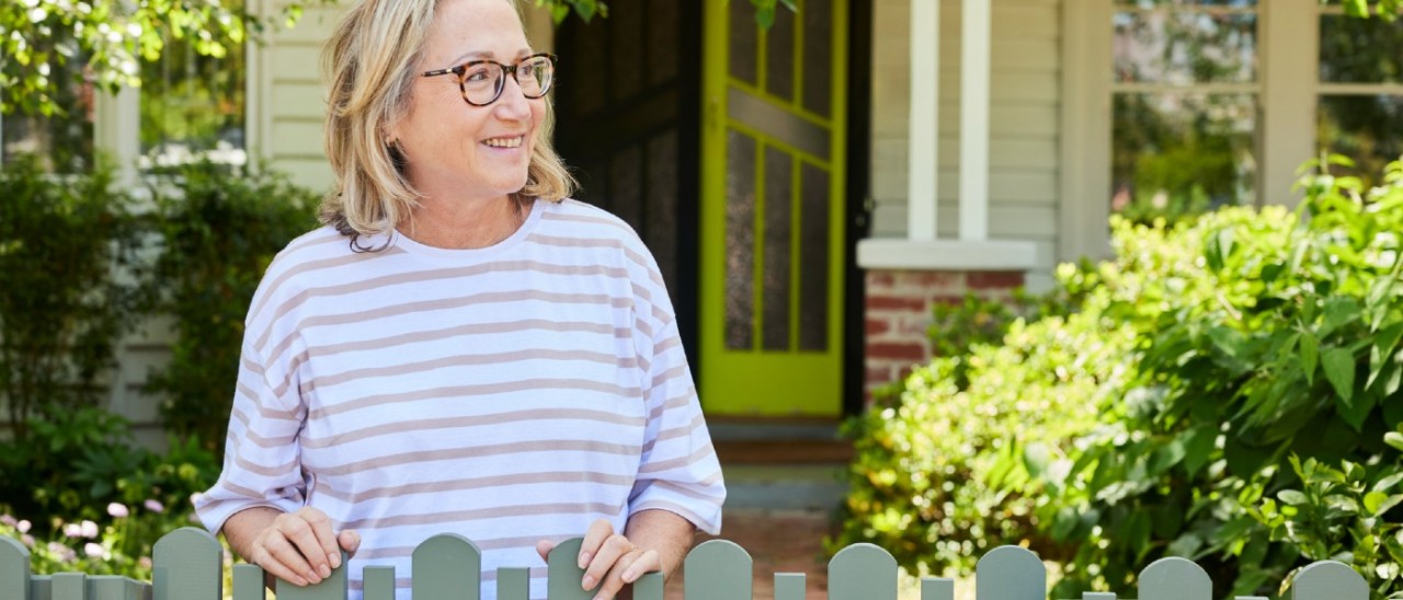 A middle-aged woman smiling as she leans on her front garden fence