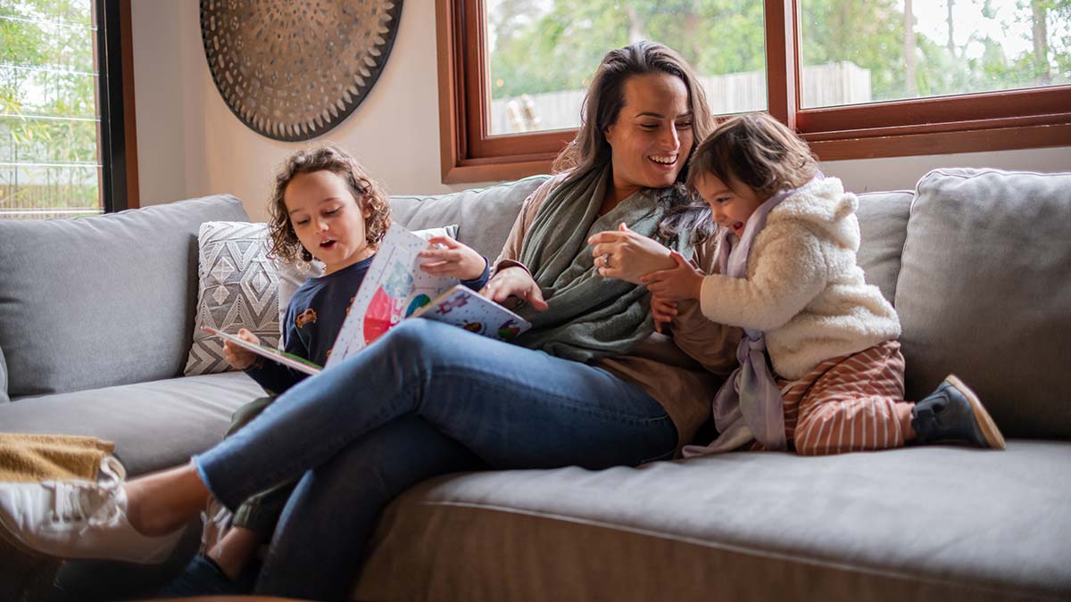 Mother and two children on couch laughing and reading books.