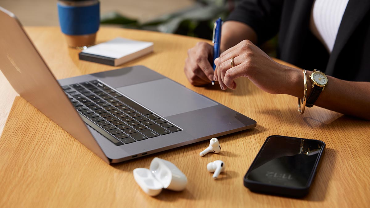 Detail shot of woman at computer showing keyboard, phone, earbuds and jewellery