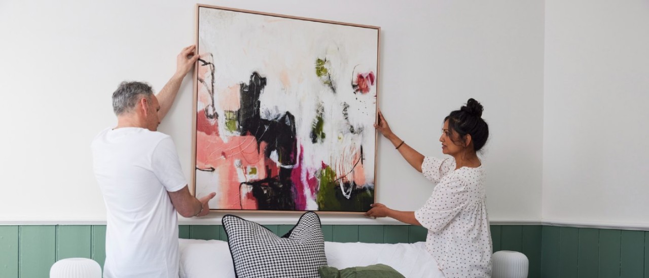 man and woman hanging a painting over a bed