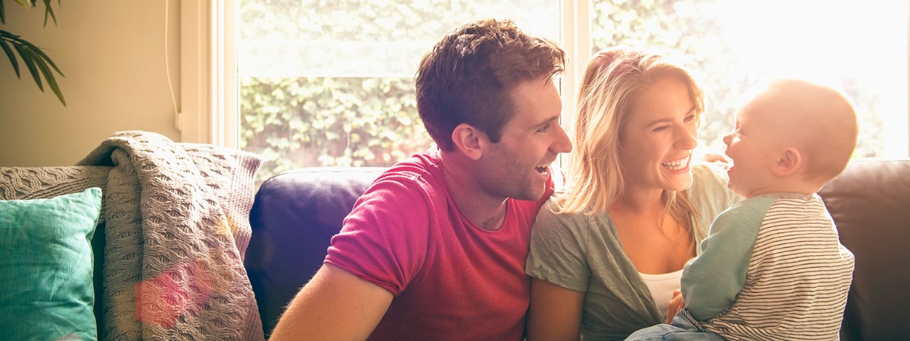758281347 Couple with baby sitting on couch next to window
