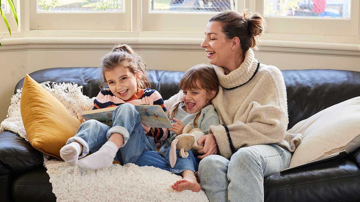 Mother with two young daughters on couch having fun with toys and books